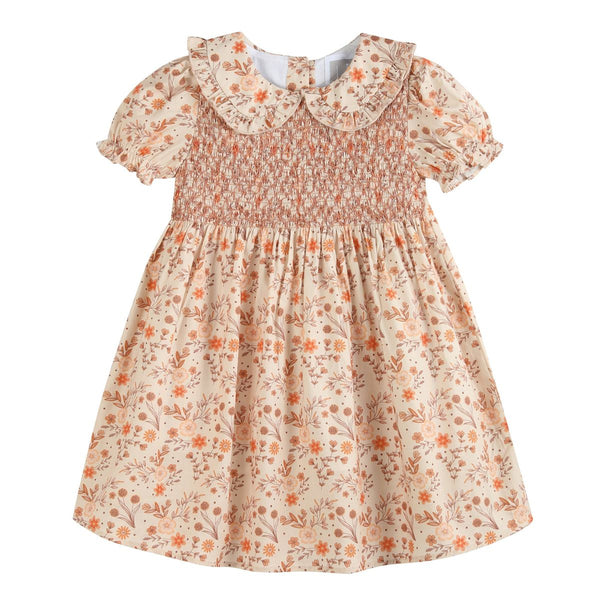 A short-sleeve baby girl's dress with a smocked bodice, a large ruffled Peter Pan collar, and an all-over floral print in orange, brown, and beige on a cream background.